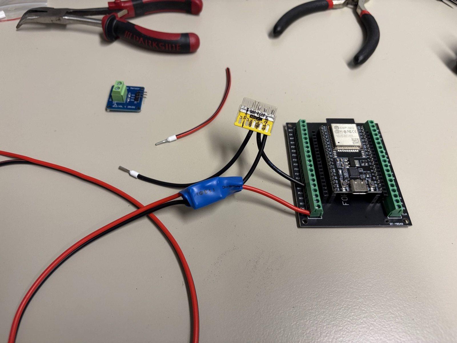 On the bench before installation: the ESP32 on a screw-terminal board, the blue 0–25 V voltage-sensor module, a Wago connector and the red and black 12 V feed.