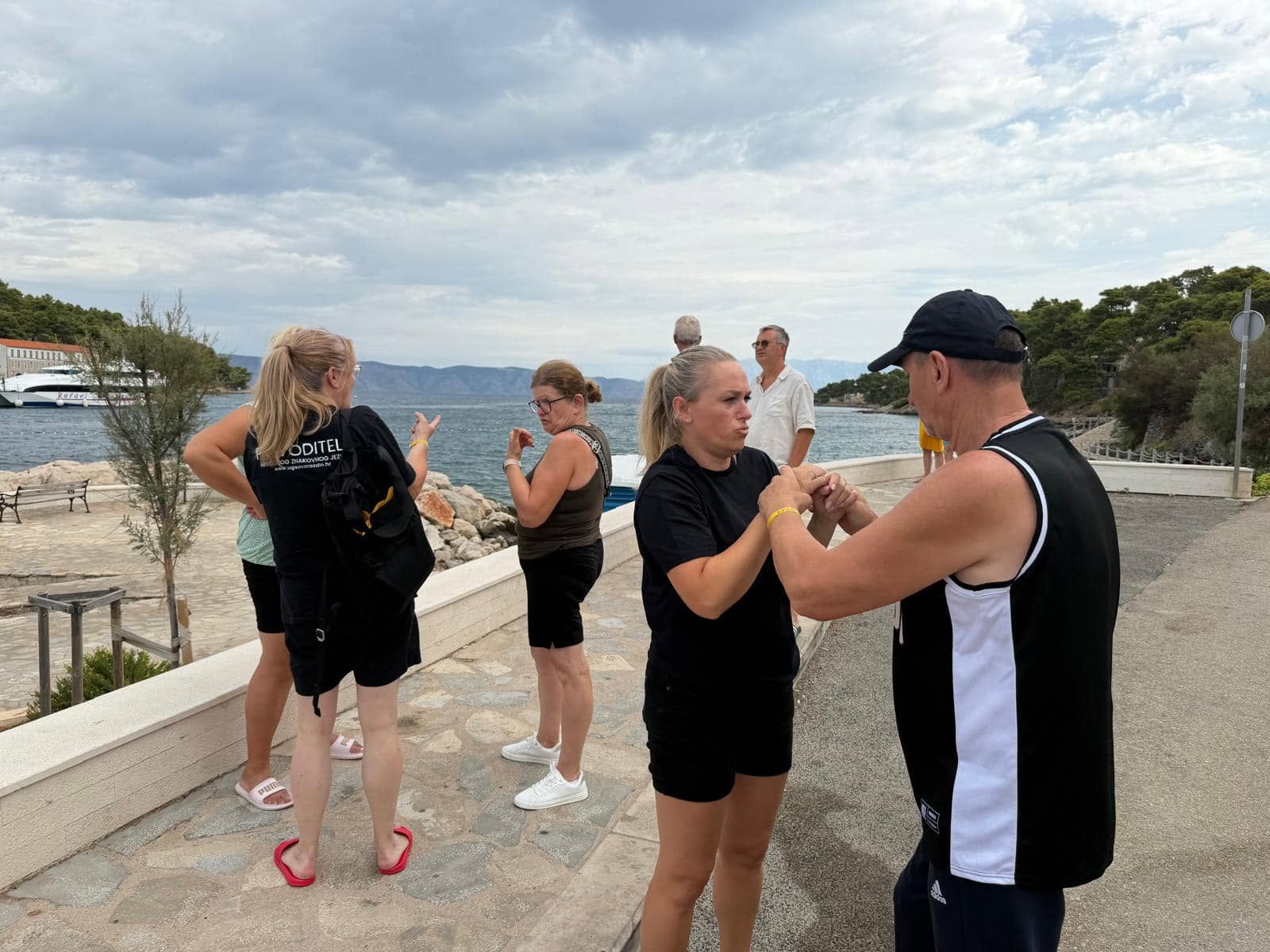 Two people communicating through touch during a seaside outing while others talk nearby.