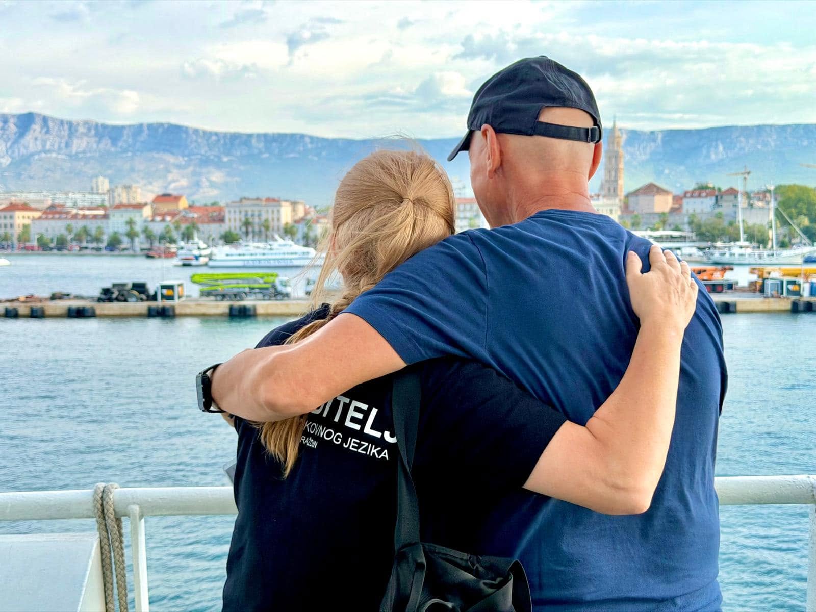 Two people standing together on a boat overlooking the waterfront.